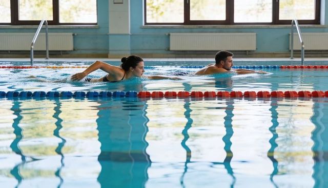 Fitness couple training breaststroke in indoor lap pool with lane ropes and reflections