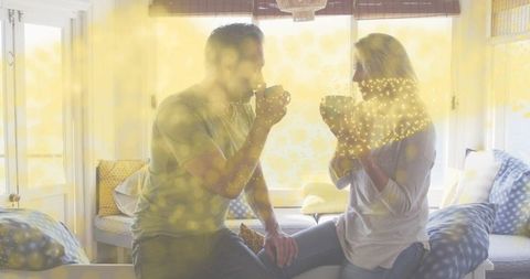 Couple sipping morning coffee on sunlit window seat, cozy home conversation