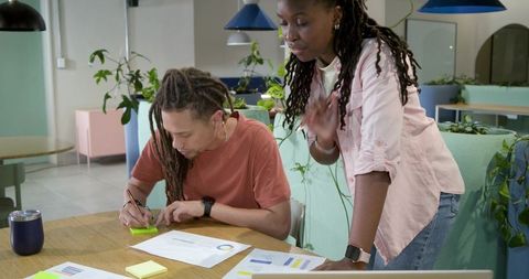African american coworkers collaborating over charts and notes in pastel coworking space