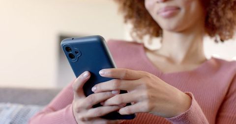 Young woman holding teal smartphone and scrolling on sofa, soft lighting, minimalist living room