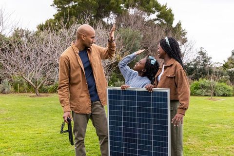 African american family installing solar panel in backyard celebrating high-five