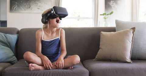 Young girl experiencing virtual reality headset on couch at home reacting with surprise