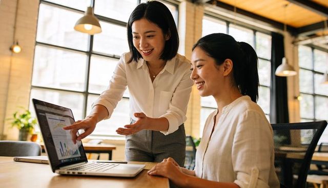 Female Colleagues Collaborating on Data Visualization Dashboard on Laptop in Loft Office