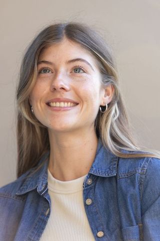 Smiling woman looking up in denim shirt with silver hoop earrings, bright portrait