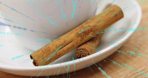 Cinnamon sticks resting in white ceramic bowl with teal paint splashes on wooden surface