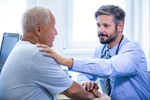 Doctor placing hand on elderly patient's shoulder while discussing medical concerns. Ideal for illustrating topics on healthcare, patient support, medical consultations, senior care, and doctor-patient relationships. Suitable for healthcare websites, medical blogs, hospital brochures, and educational materials.