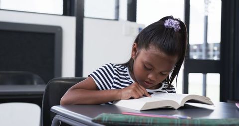 Young Girl Engrossed in Reading at School Desk