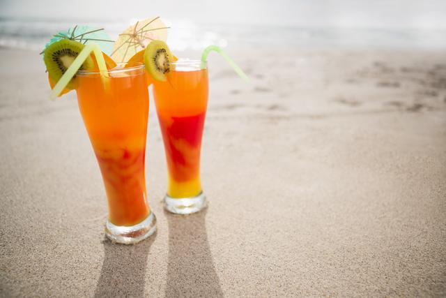 Two glasses of cocktail drink kept on sand at tropical beach