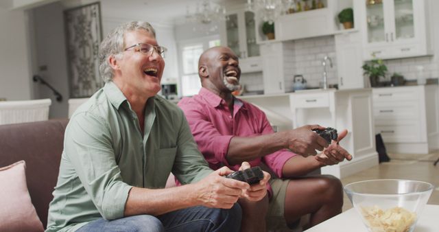 Two senior men are playing video games and laughing in living room fully engaged in their game. This can be used to depict active lifestyles for older adults, friends bonding, and leisure activities in home settings.