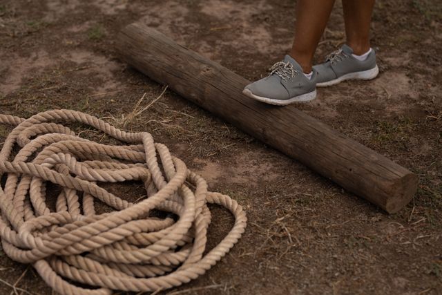 Low section of Caucasian woman at a boot camp training session, exercising, with one foot on a log, rope next to her. Outdoor exercise, fun healthy challenge.