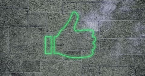 Neon green thumbs-up on brick wall symbolizing approval