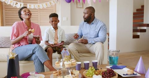 African American family celebrating birthday at home laughing and sharing cupcakes