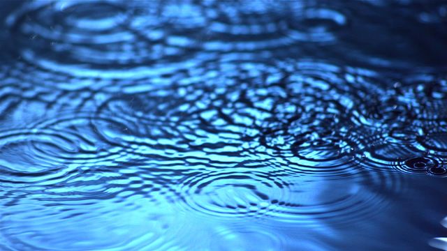 Close-up of raindrops creating ripples on water surface, showcasing serene and calm moment with concentric circles reflecting beautifully in blues. Ideal for use in calming and serene themed designs, nature compositions, water-related content or background, relaxation and tranquility visuals, and environmental awareness campaigns.