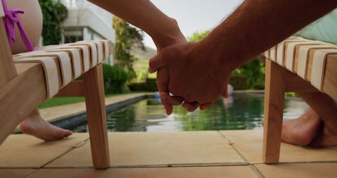 Couple Holding Hands on Sun Loungers by Swimming Pool