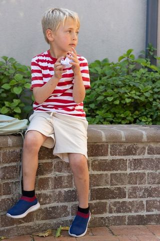 Young boy sitting on brick wall holding crumpled paper looking thoughtful in courtyard