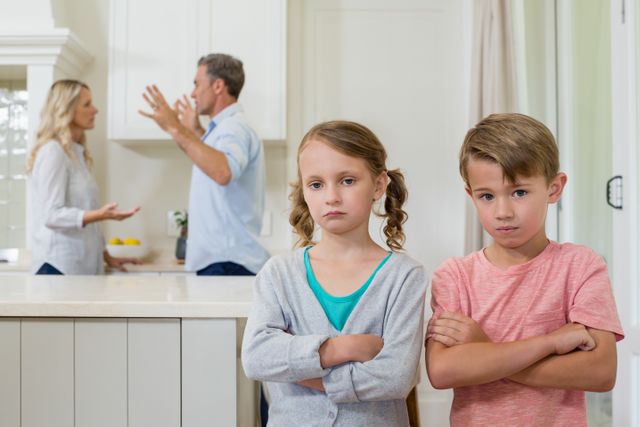 Sad siblings standing with arms crossed while parents arguing in background. This image can be used to depict family conflict, emotional distress in children, and the impact of parental arguments on kids. Suitable for articles, blogs, and campaigns related to family issues, mental health, and child psychology.