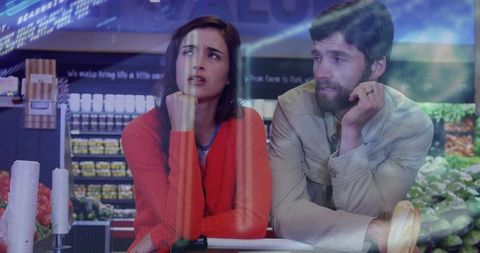 Young couple leaning on grocery counter looking thoughtful in supermarket produce aisle