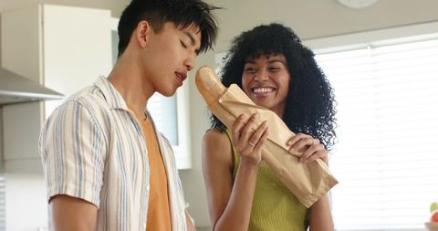 Smiling mixed-race couple sharing fresh baguette in bright modern kitchen