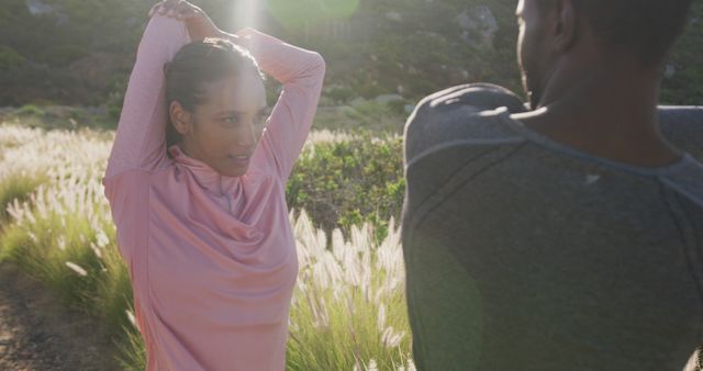 Diverse couple performing stretching exercises in a green field, enveloped by natural light. Scene emphasizes a commitment to fitness and well-being through outdoor activities. Ideal for illustrating healthy lifestyles, viral fitness Instagram posts, or promoting community exercise programs.