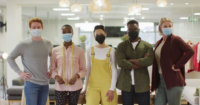Diverse team of colleagues standing together in an office environment, all wearing face masks for protection. This image is perfect for illustrating concepts such as workplace diversity, team collaboration during COVID-19, and safety precautions in a work setting.