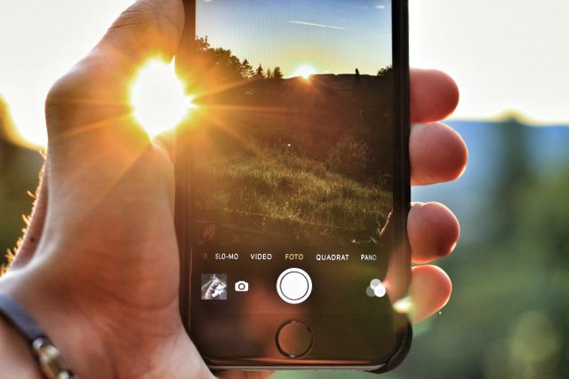 Person using smartphone to capture sunset over nature. Ideal for themes around technology, outdoor photography, moments, travel applications, mobile shooting techniques, capturing memories, and documenting life experiences.