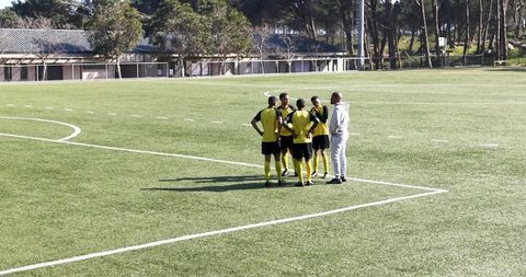 Soccer Coach Diagramming Plays with Team on Field