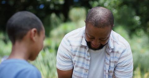 African american father and teenage son sharing warm smile and bonding outdoors in park