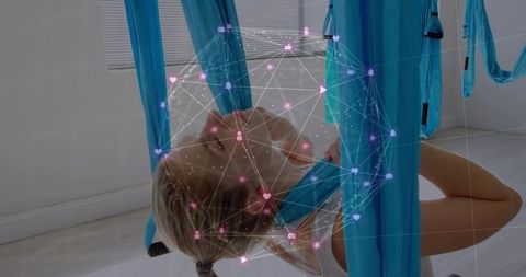 Practicing aerial yoga in blue silks with digital network overlay for wellness