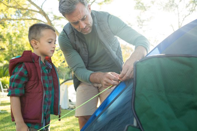 Father and son setting up a tent at a campsite on a sunny day. Ideal for use in articles or advertisements about family bonding, outdoor activities, camping trips, and parenting. Perfect for promoting camping gear, family vacations, and nature excursions.