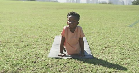 Smiling African American Boy Practicing Yoga on Grass Mat