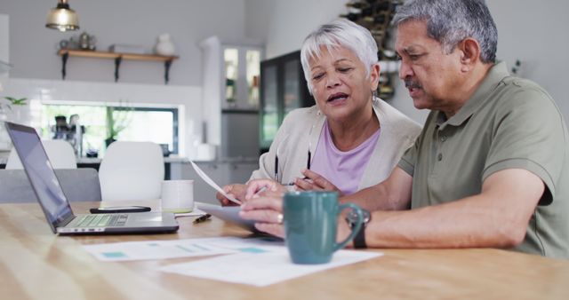 Happy senior biracial couple talking and using laptop. Spending quality time at home, retirement and lifestyle concept.