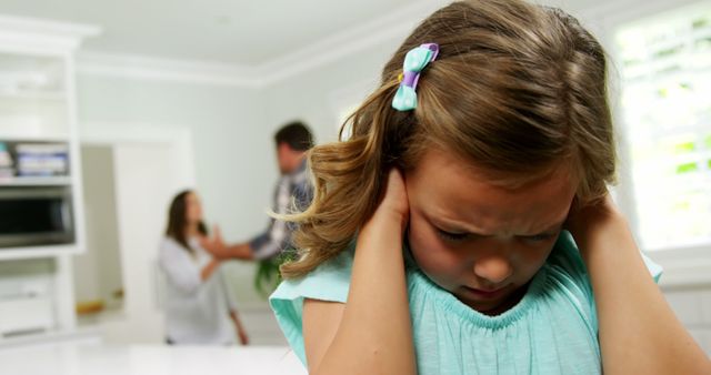 Young girl closing her ears, appearing upset while her parents argue in the background. Useful for illustrating themes related to family conflict, emotional distress in children, domestic issues, and the impact of parental arguments on children. Suitable for articles, presentations, or counseling materials focusing on family relationships and child welfare.
