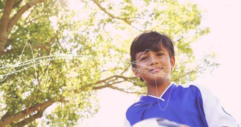 Smiling boy holding soccer ball under sunlit tree, posing with light streaks and copy space