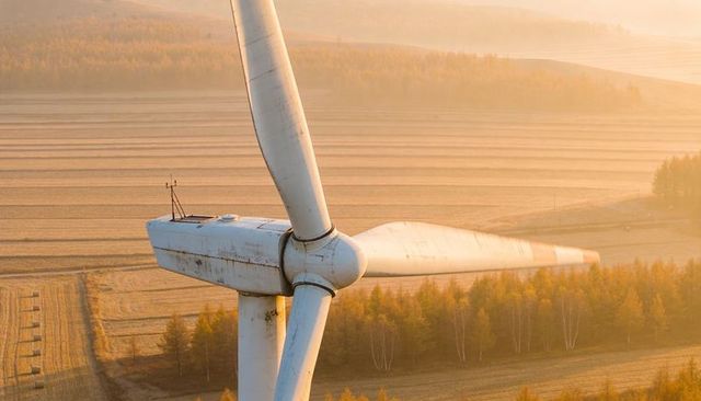 Towering wind turbine nacelle and rotor overlooking golden fields in autumn sunrise