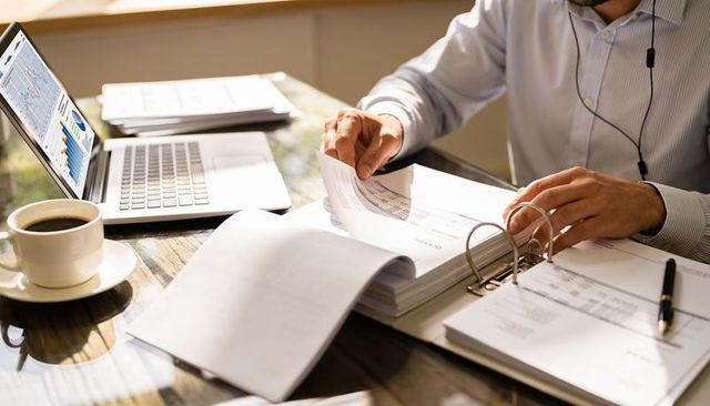 Business professional reviewing financial reports and charts with laptop, binder, coffee