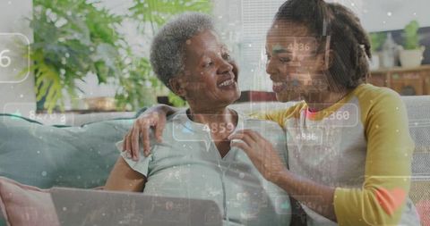 Adult daughter helping older mother with laptop while sharing warm couch connection