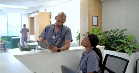 African american nurse and doctor reviewing tablet at modern clinic reception desk