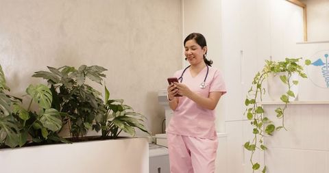 Nurse using smartphone in modern clinic with indoor plants and relaxed waiting area