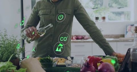 Female pouring olive oil over fresh vegetables with ar sustainability icons in kitchen