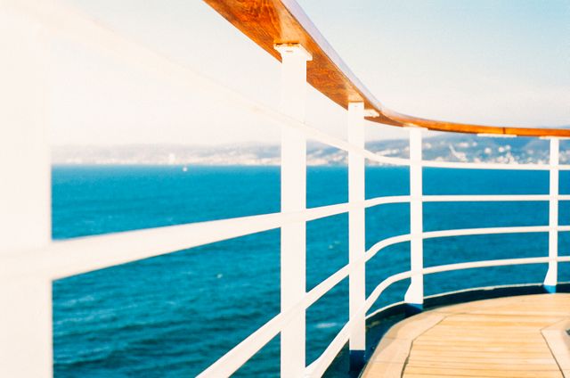Picture illustrating the railing of a cruise ship deck with a vast ocean view and clear blue skies. Ideal for tourism marketing, travel blogs, advertisements promoting cruise vacations, and luxury getaways.
