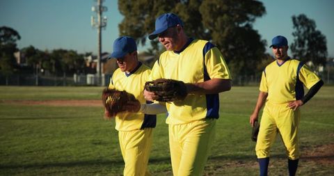 Competitive baseball teammates walking across field in bright yellow uniforms and gloves