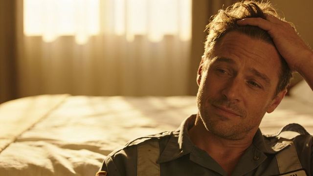 Sunlit contemplative worker relaxing on bed in uniform running hand through hair