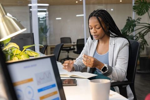 African american professional woman taking notes at modern workspace wearing smartwatch