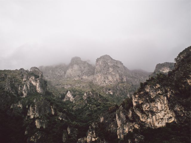 Dramatic landscape of misty mountain range with rugged cliffs and lush green vegetation. Perfect for travel blogs, nature documentaries, outdoor adventure promotions, and environment-focused content.