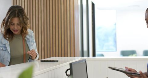 African american client checking phone at reception counter while staff using tablet