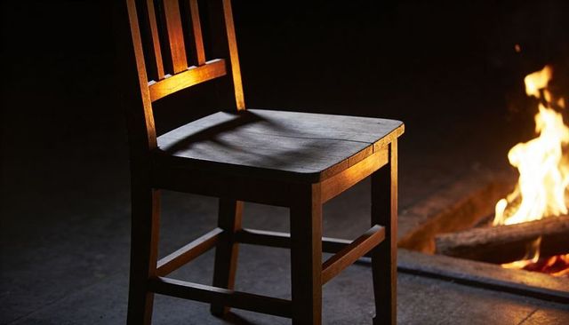 Rustic wooden chair bathed in firelight casting deep shadows and glowing embers
