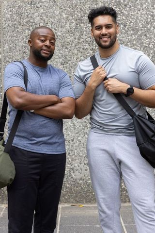 Two male friends smiling and carrying duffel bags on urban sidewalk in gym wear
