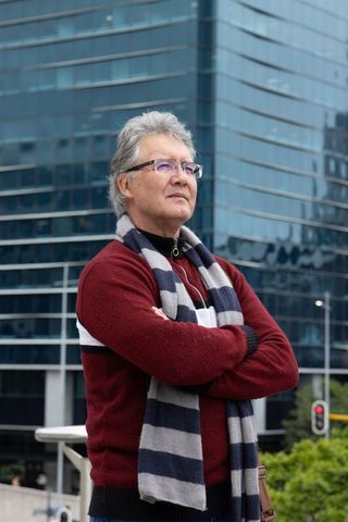 Confident senior man in maroon sweater and striped scarf standing with arms crossed in downtown