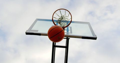 Basketball Swishing Through Outdoor Hoop Against Cloudy Sky