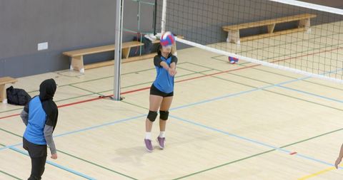 Indian athlete bumping volleyball during indoor practice wearing hijab knee pads blue top